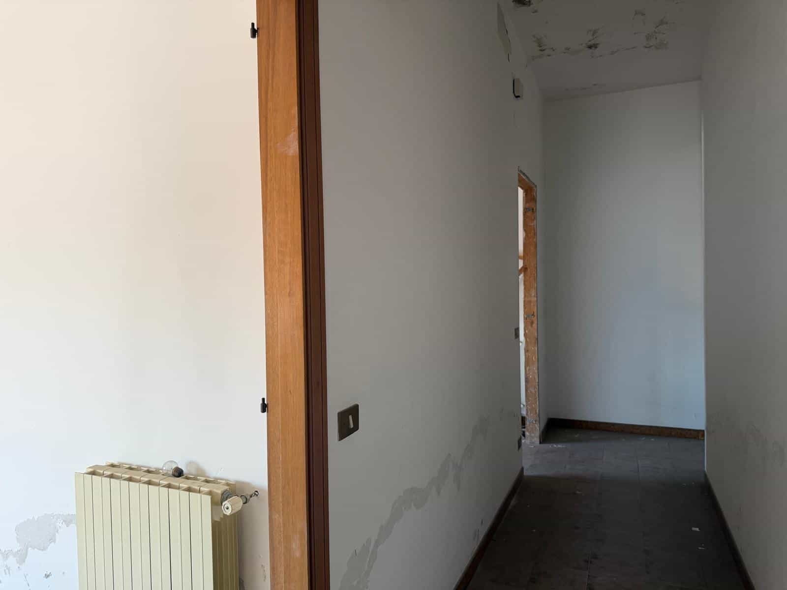 Ampia vista di un corridoio in fase di ristrutturazione con pareti bianche e pavimento in cemento, pronto per essere personalizzato e arredato. Ideale per progetti di ristrutturazione e interior desig.