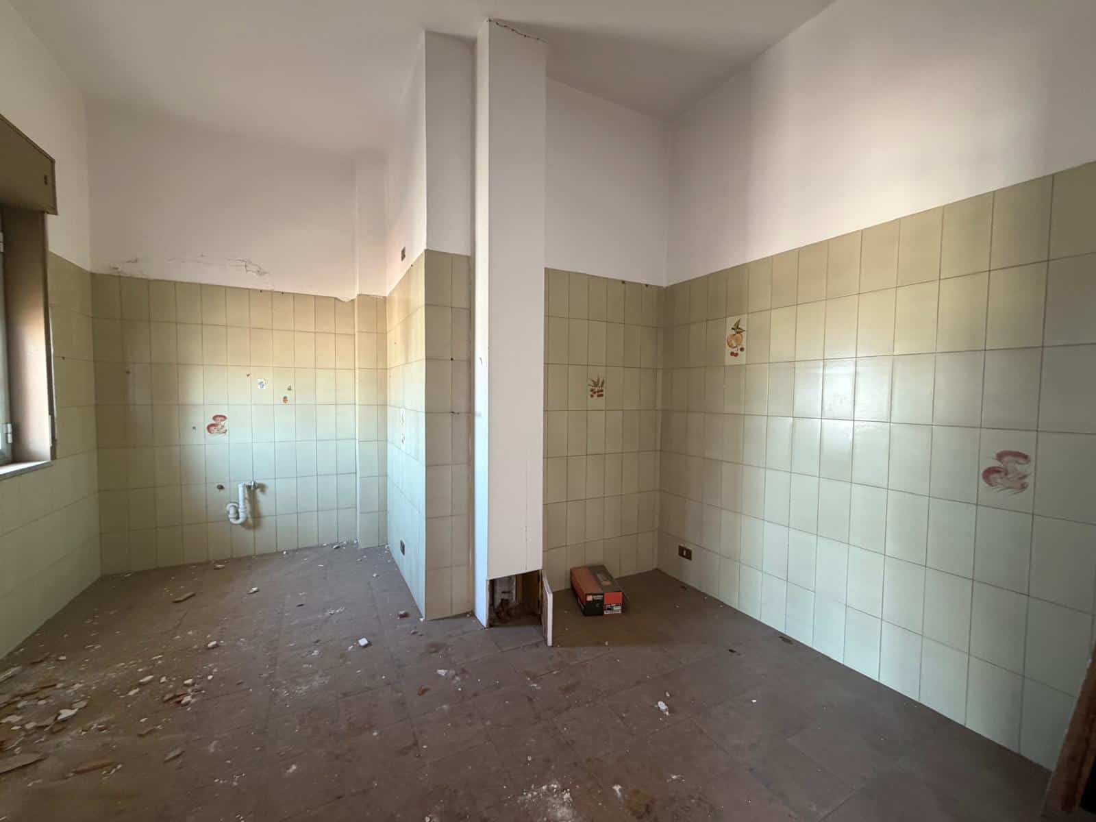 Lavanderia in fase di ristrutturazione con pareti rivestite di piastrelle beige e pavimento in cemento, pronta per essere trasformata in uno spazio funzionale e moderno.