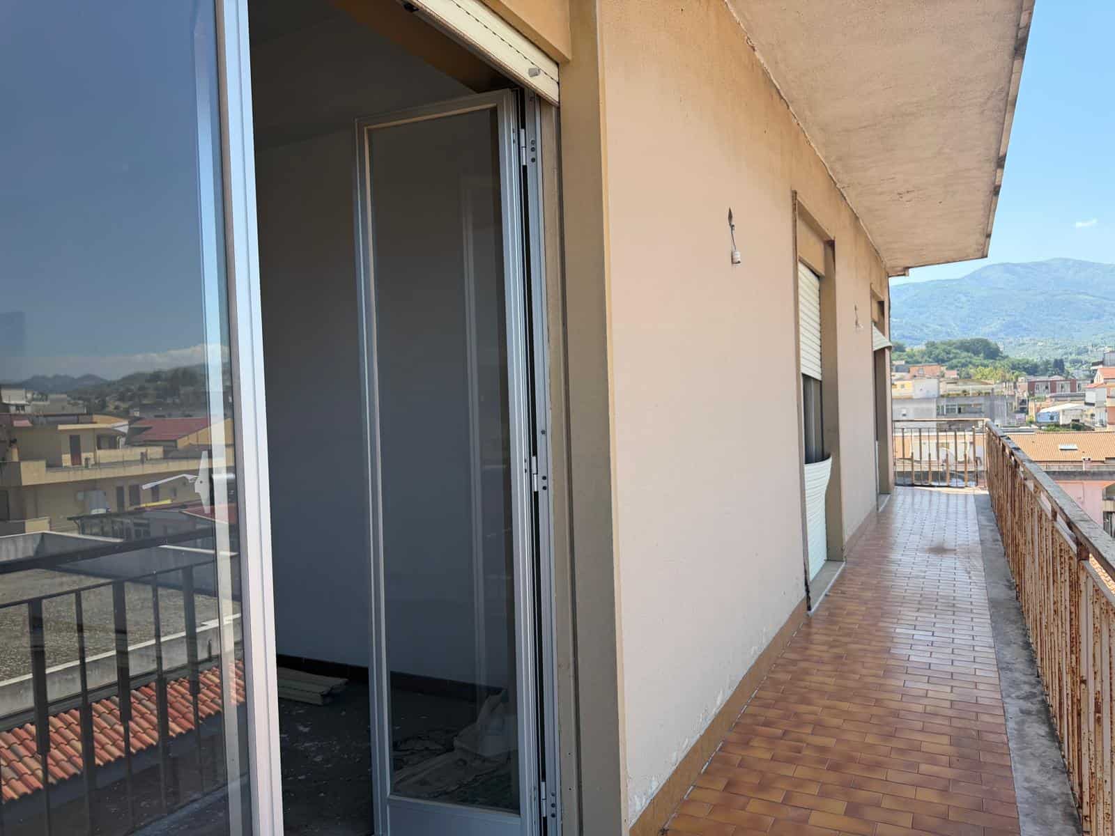 Ampia terrazza con vista panoramica su città e montagne, ideale per relax e socializzare, con pavimentazione in piastrelle e ringhiera in ferro. Perfetta per appartamenti in vendita o affitto a NextCa.