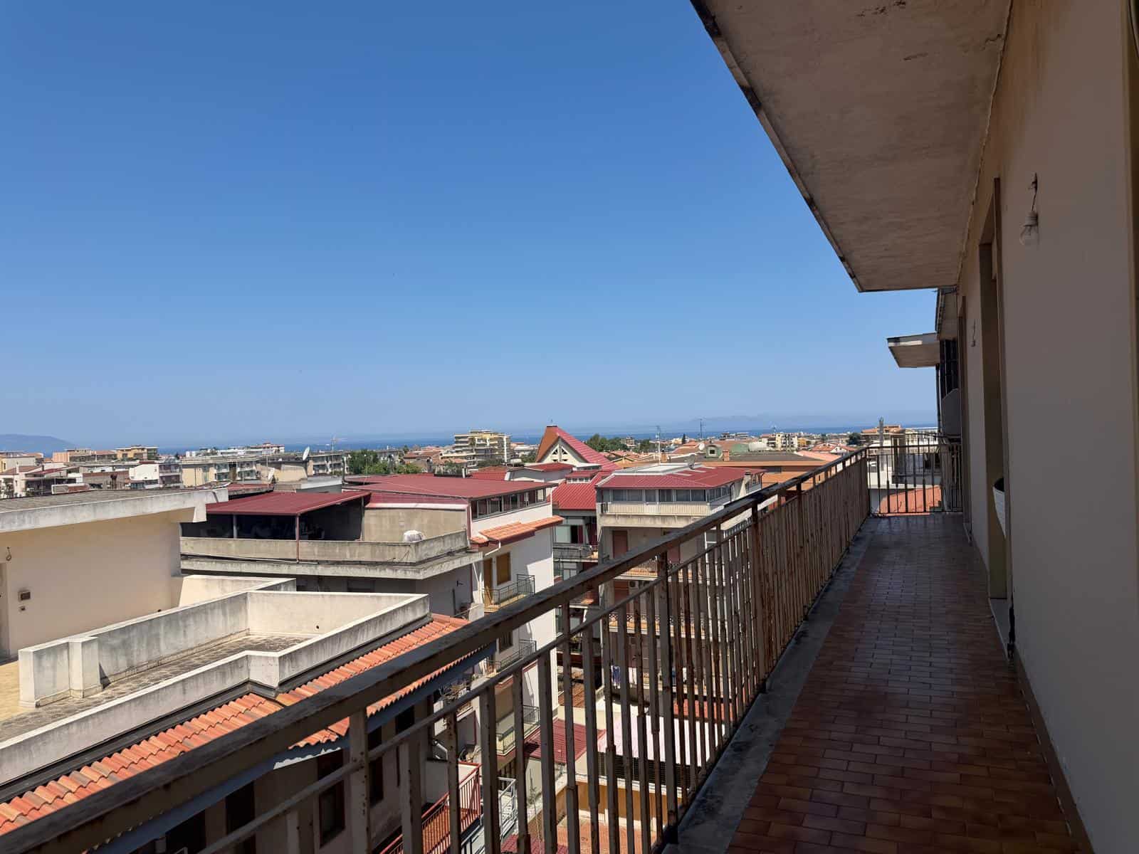 Balcone di un appartamento con vista panoramica sulla città e il mare in lontananza, in un contesto urbano mediterraneo.