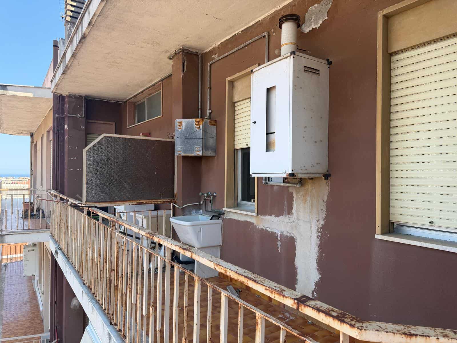 Facciata di un edificio residenziale con balcone, infissi e impianti esterni, in condizioni di usura e manutenzione da migliorare.