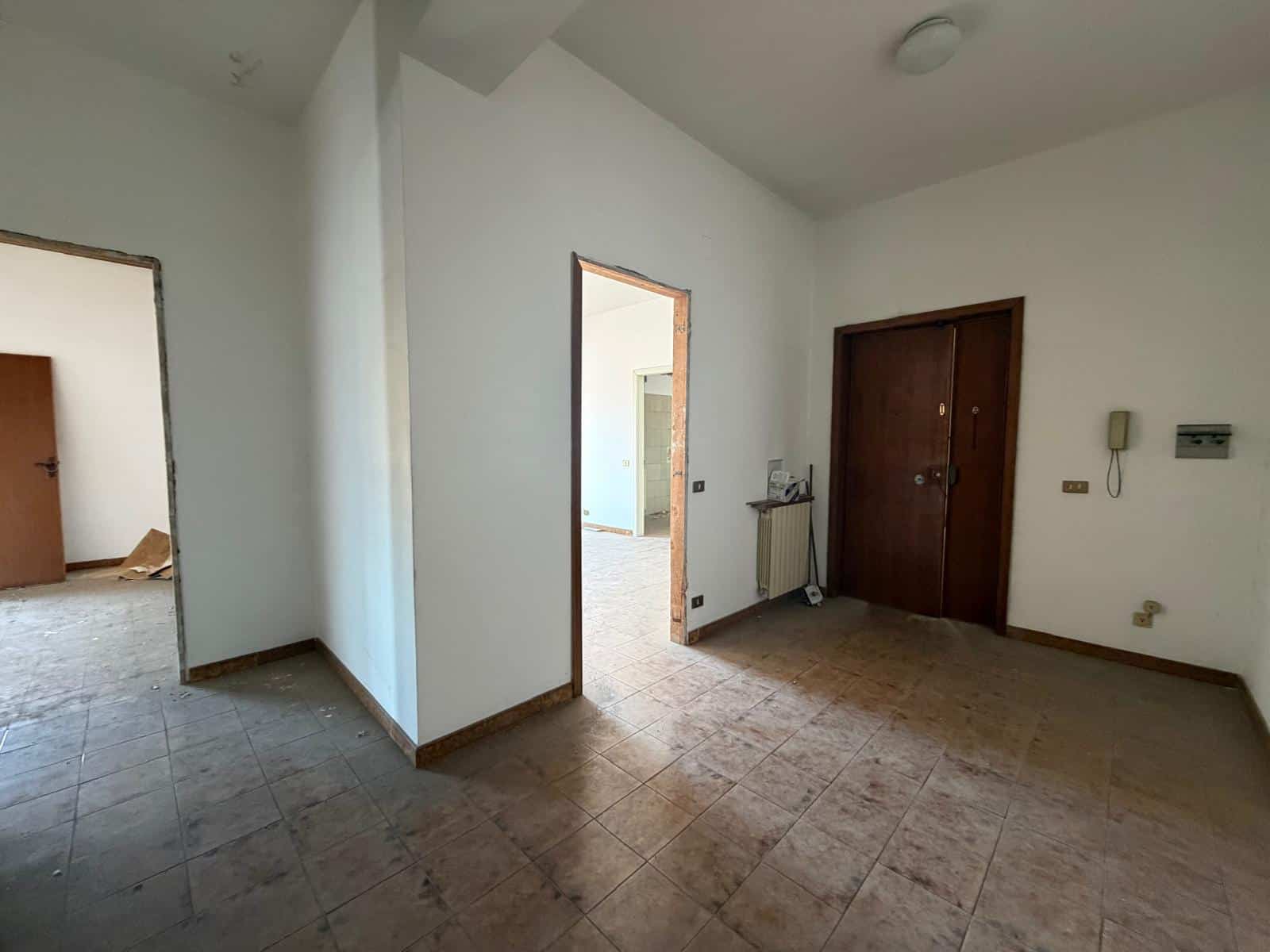Interno di un appartamento vuoto con pareti bianche, porte in legno e pavimento in piastrelle, pronto per essere arredato.