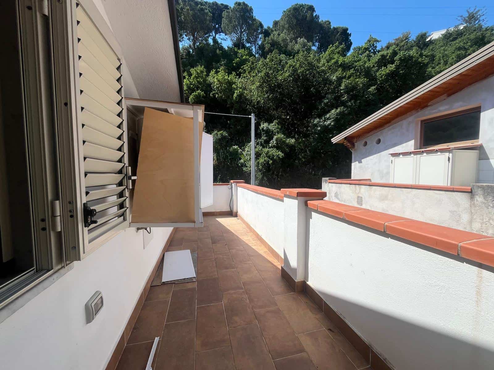 Ampio balcone con ringhiera in muratura e vista su verdeggiante area boschiva, ideale per relax e momenti all'aperto.