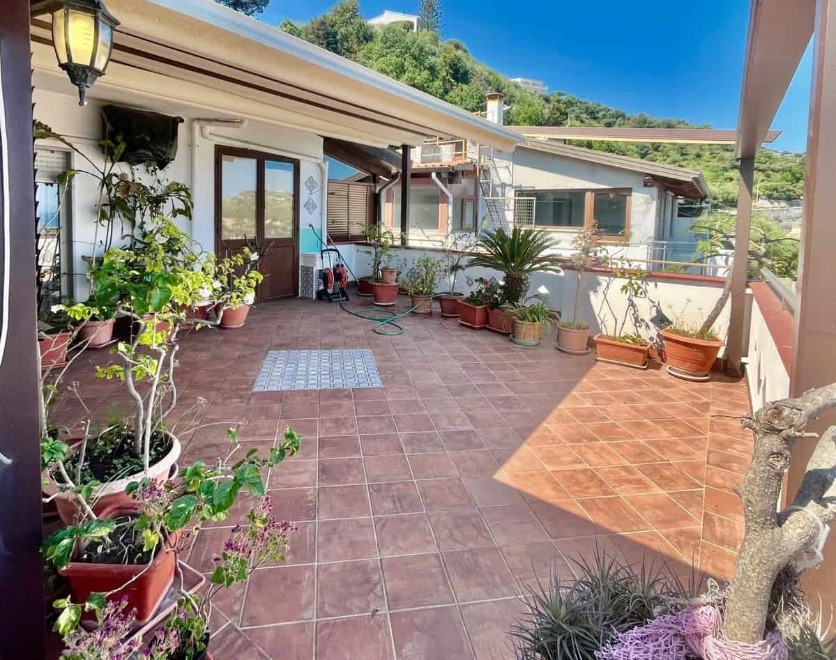 Ampio terrazzo esterno con piante in vaso, vista su colline verdi e cielo sereno, ideale per relax e convivialità, in zona residenziale tranquilla.