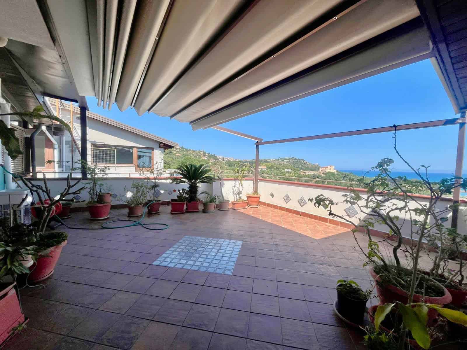 Ampia terrazza con vista panoramica sul mare e sulla costa, decorata con piante in vaso e arredi moderni, ideale per relax e intrattenimento all'aperto.