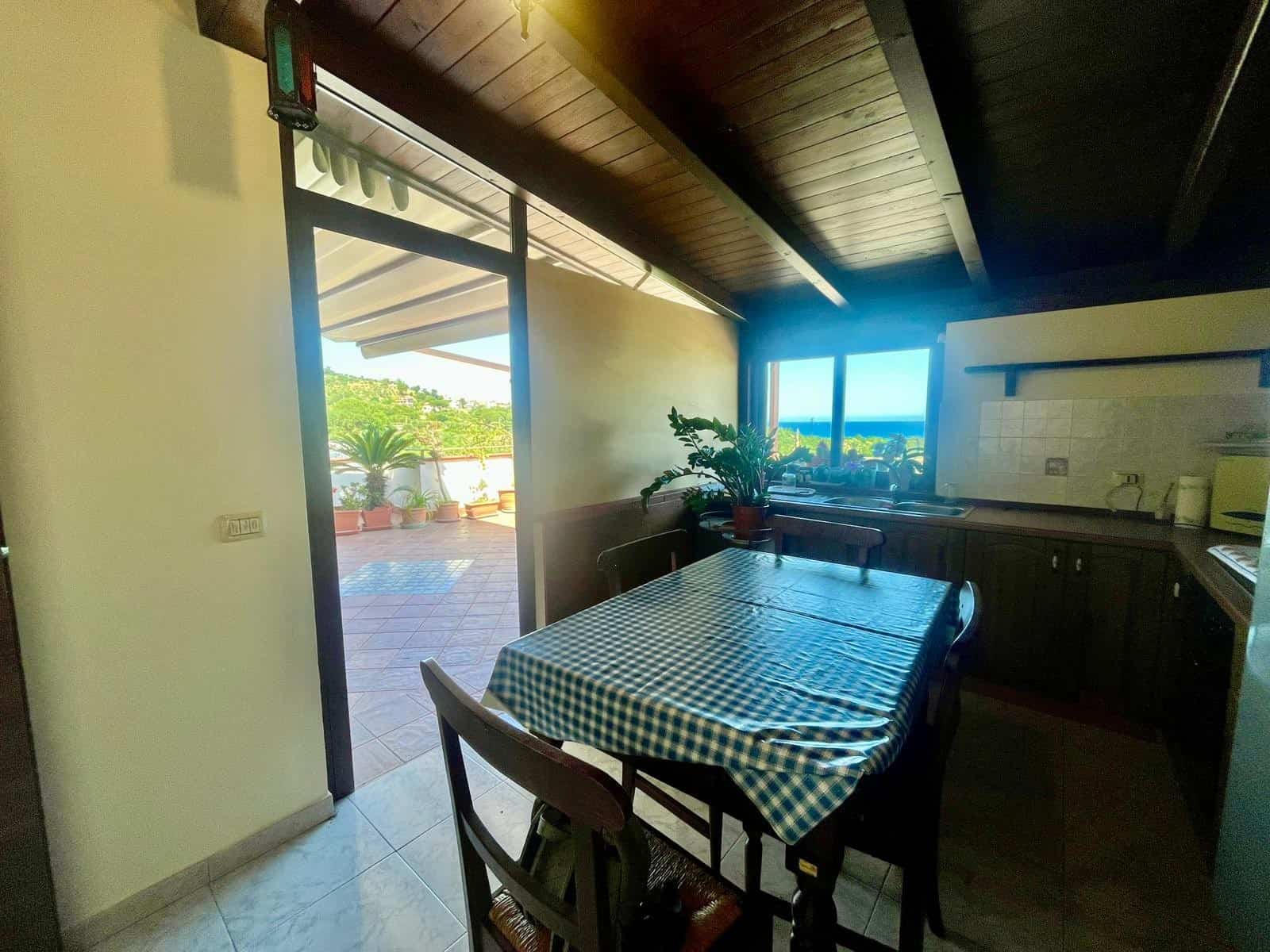 Ampia sala da pranzo con tavolo a quadretti blu e bianco, accesso a terrazza con vista panoramica, cucina moderna con mobili scuri, ambiente luminoso e accogliente, ideale per soggiorni rilassanti.