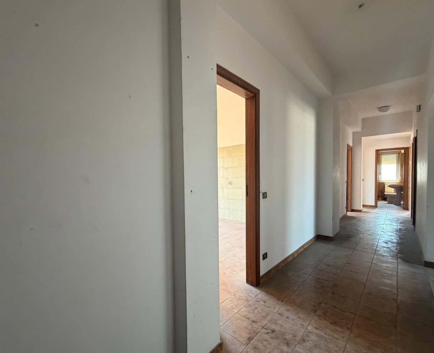 Corridoio interno di un appartamento in fase di ristrutturazione, con pareti bianche e pavimento in piastrelle, pronto per essere arredato.