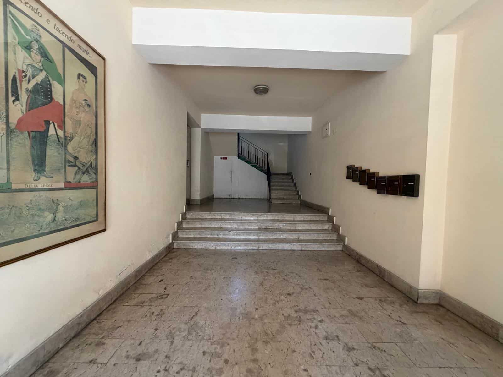 Ampia zona di ingresso condominiale con pareti bianche, affreschi artistici e scalinate in marmo, ideale per accogliere residenti e visitatori in un ambiente luminoso e curato.
