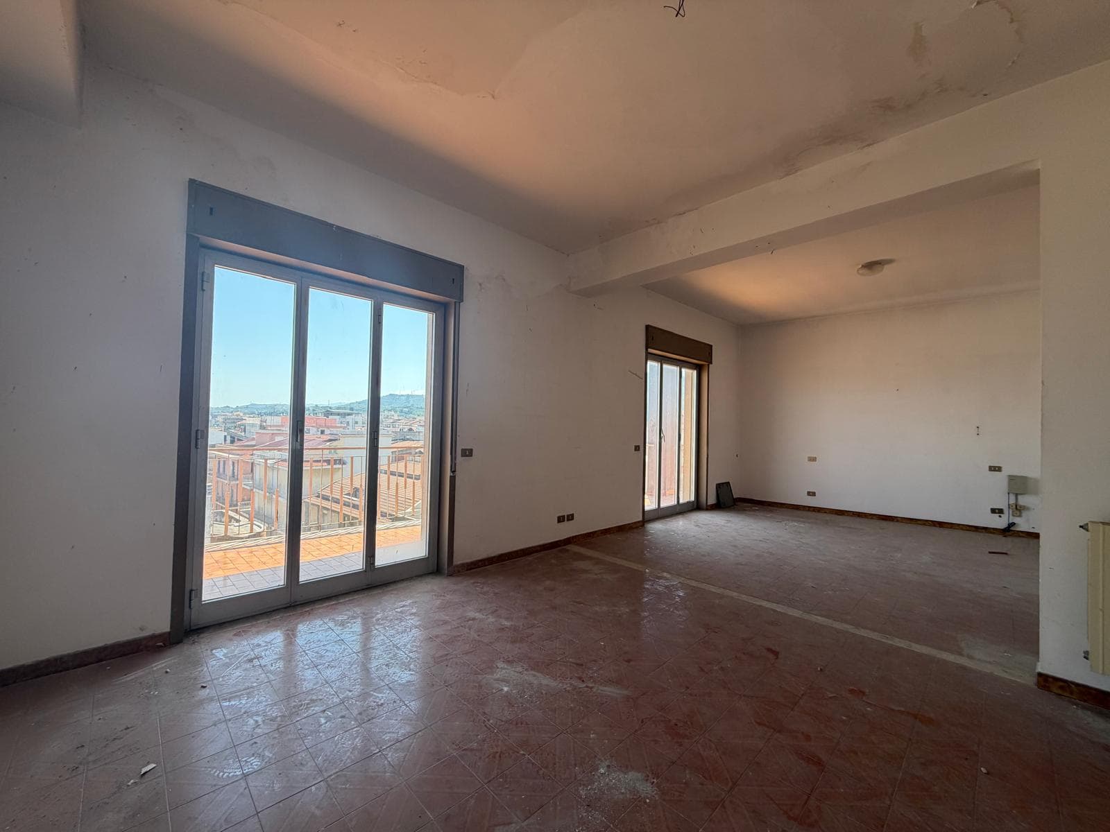 Interno di un appartamento in fase di ristrutturazione con grandi finestre e vista sulla città, pronto per personalizzazione e arredo.