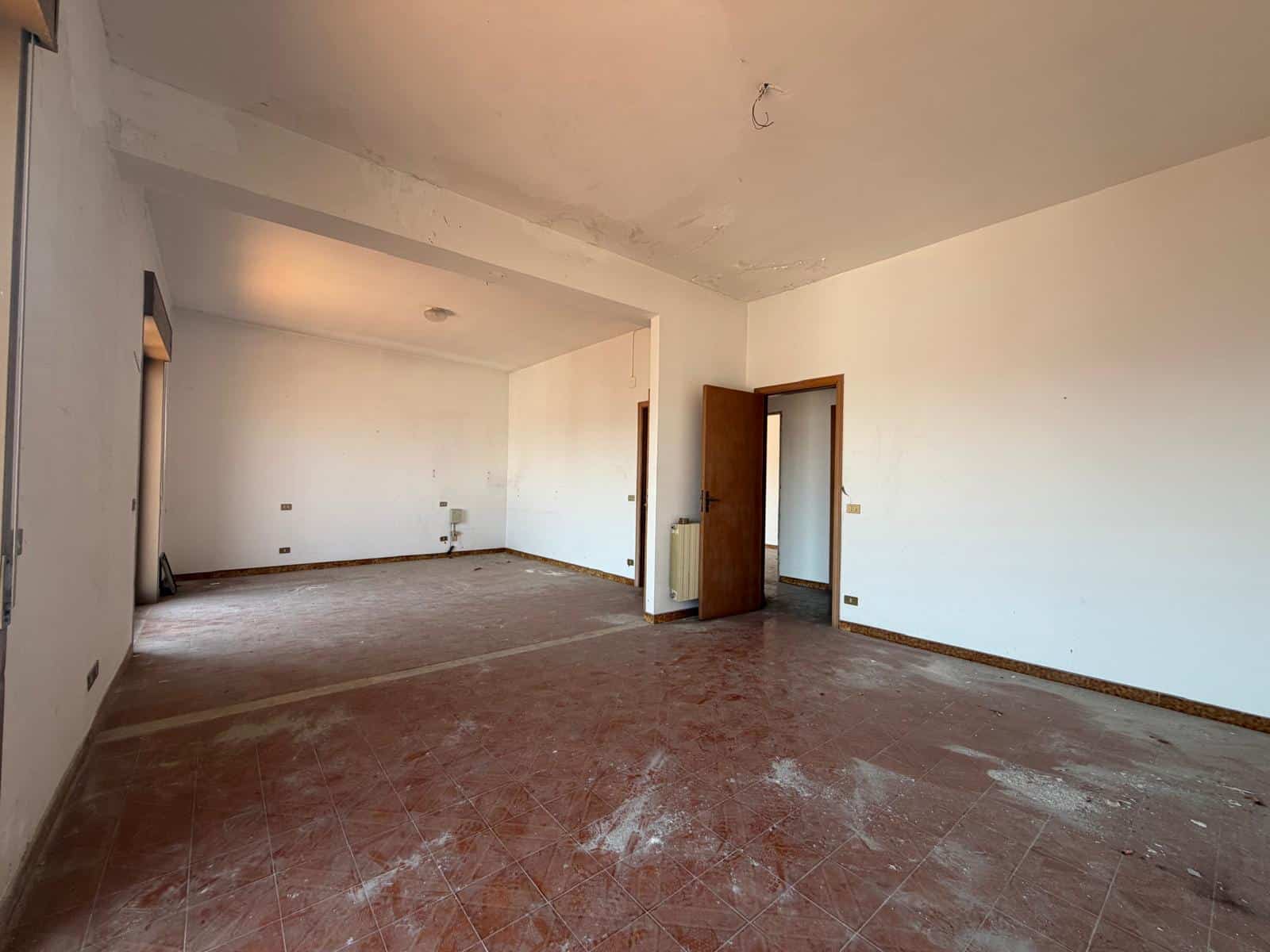 Interno di un appartamento vuoto in fase di ristrutturazione, con pareti bianche e pavimento in piastrelle rosse, pronto per essere arredato.