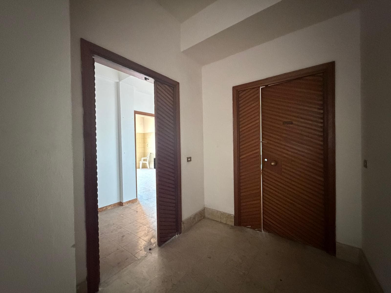Ampio ingresso con porta scorrevole in legno e pareti bianche, ideale per l'accesso a diverse stanze di una casa o appartamento. Spazio luminoso e funzionale, perfetto per creare un ambiente accoglien.