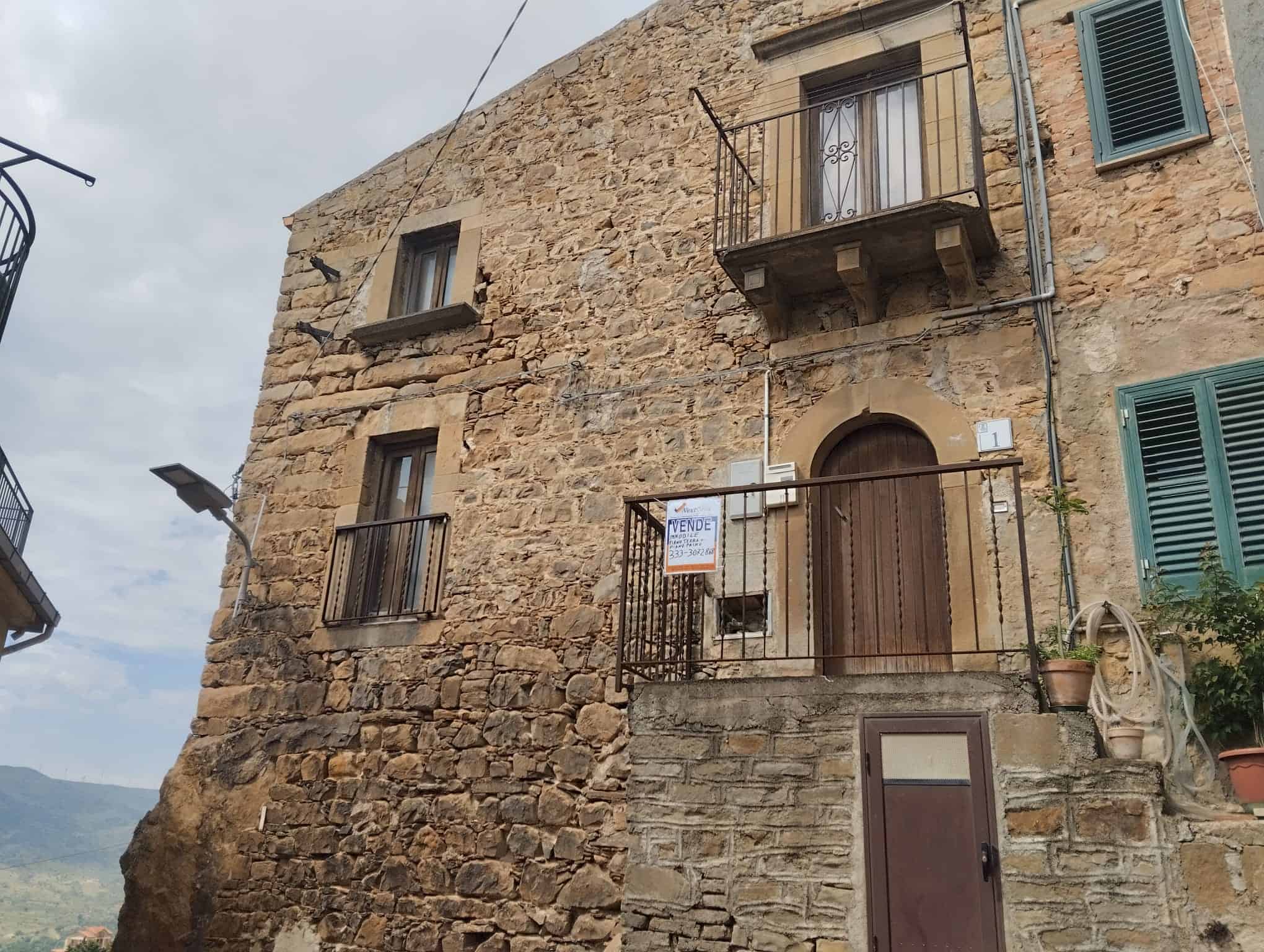 Antico edificio in pietra con balcone e finestre con persiane verdi, situato in un borgo storico toscano, perfetto per investimento immobiliare o casa vacanze in Italia.