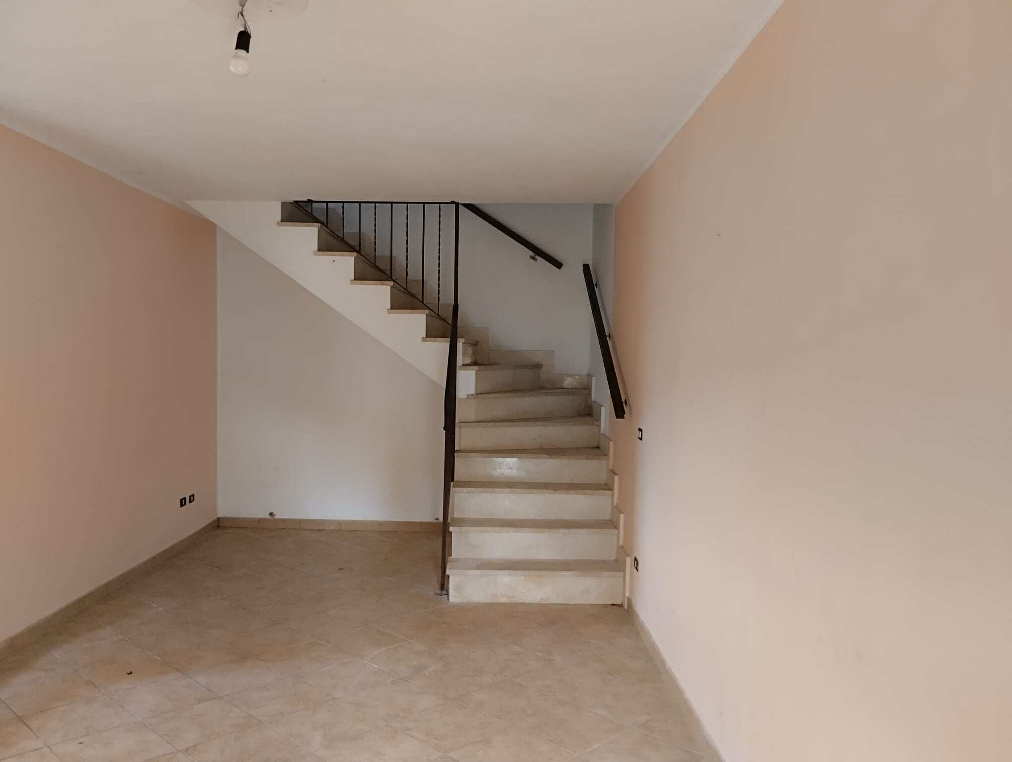 Scale interna di un appartamento con pareti neutre e pavimento in piastrelle beige, dotata di ringhiera in metallo nero e gradini in cemento, pronta per essere personalizzata.