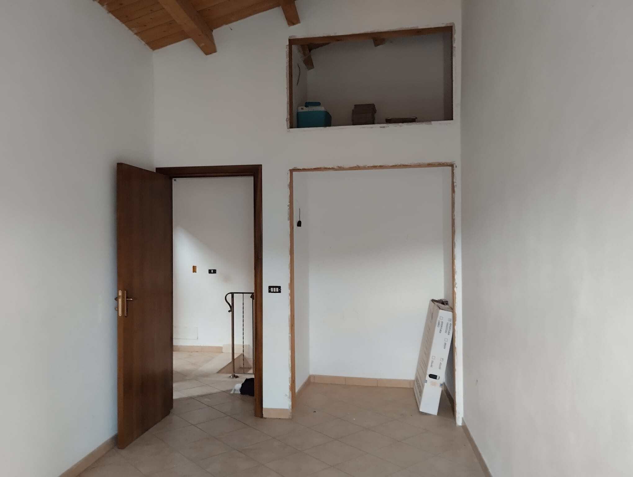 Porte in legno aperta che conduce a una stanza in fase di ristrutturazione, con pareti bianche e soffitto in legno, spazio vuoto pronto per personalizzazione e arredamento.