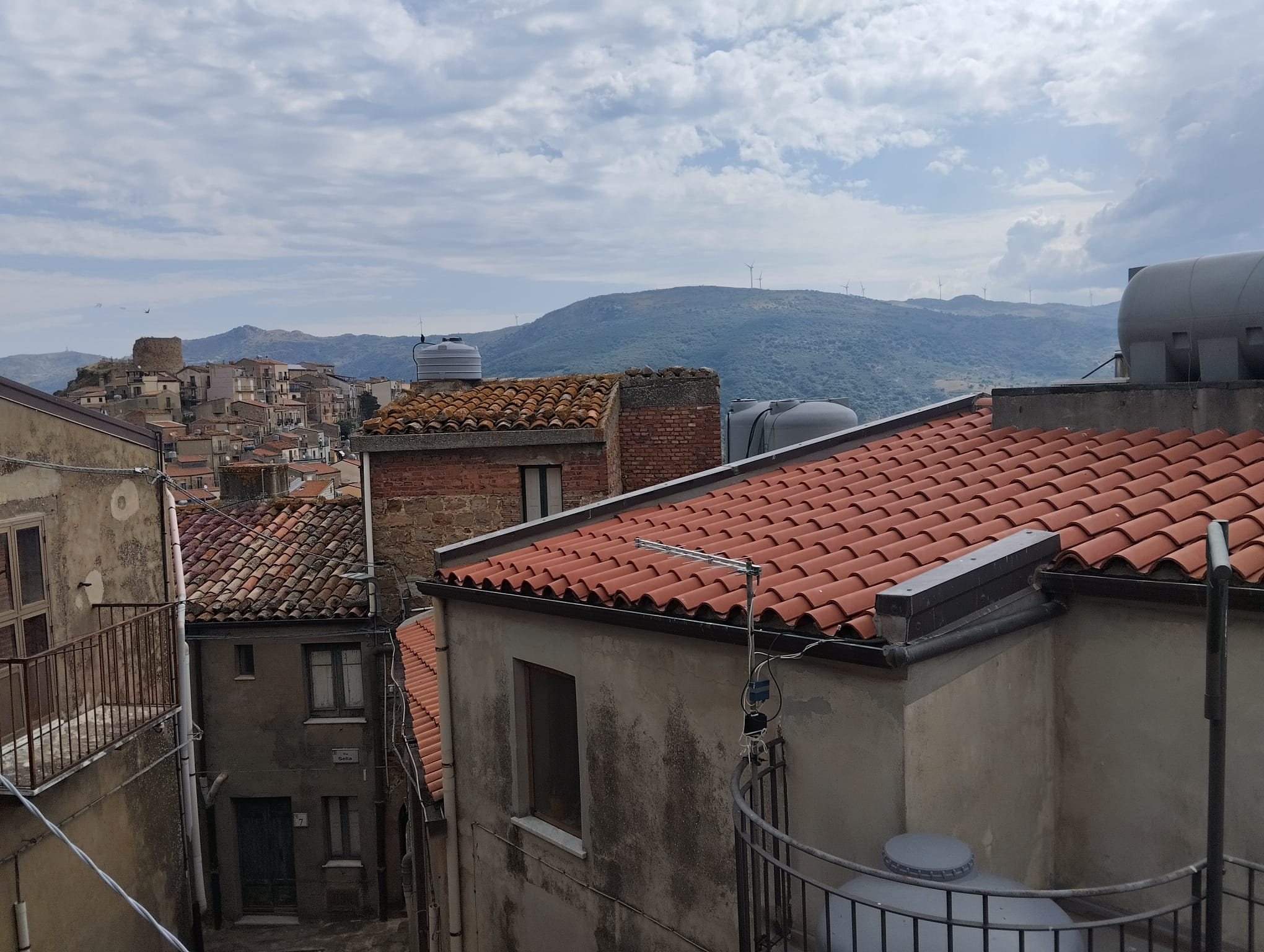 Vista panoramica sui tetti di un quartiere storico con colline sullo sfondo, cielo nuvoloso, in un ambiente urbano italiano.