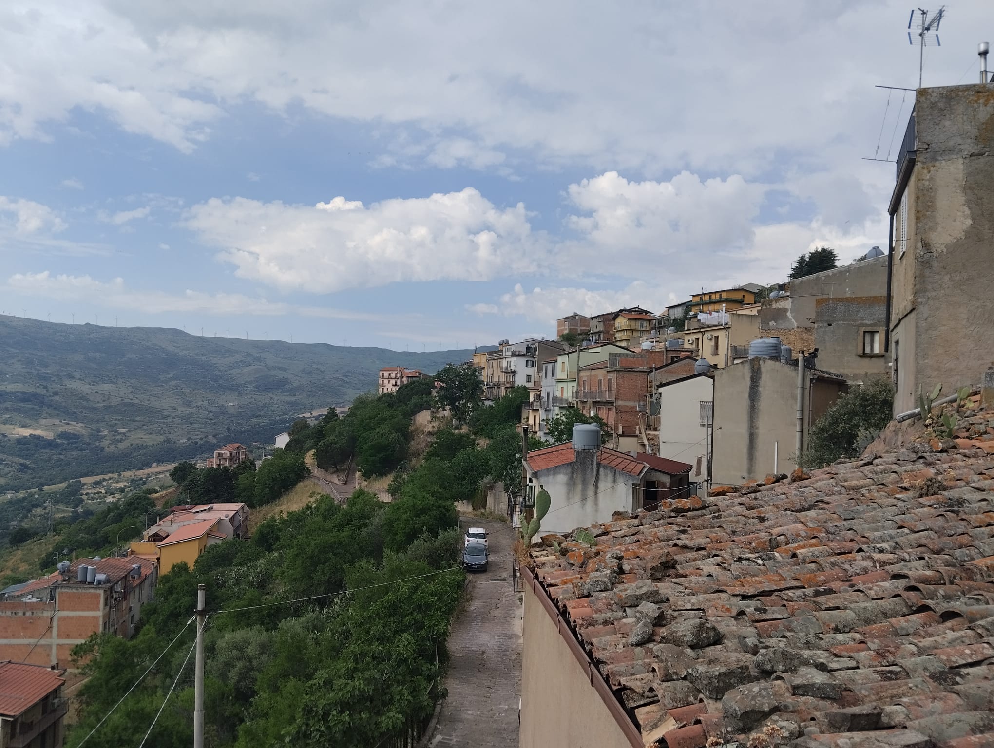 Vita di paese con case colorate e strade strette, vista panoramica sulle colline e il cielo nuvoloso, in un paesaggio rurale italiano.