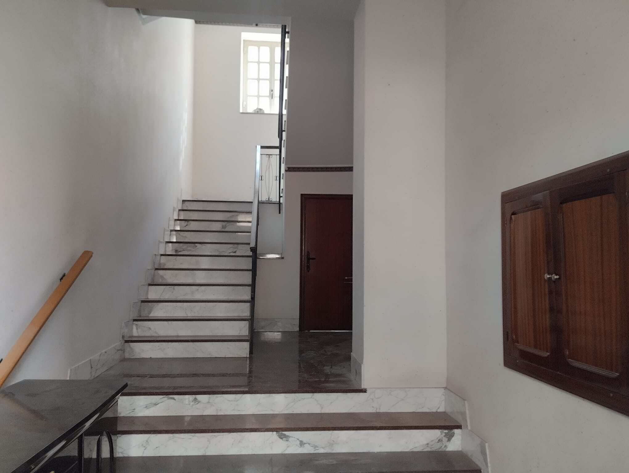 Porte interne in legno e scala in marmo bianco in un ingresso di casa con pareti bianche e finestra luminosa.