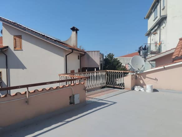 Ampio terrazzo con vista su case residenziali, parapetto in metallo e satellite, pavimentazione in cemento, ideale per relax e attività all'aperto, in zona tranquilla e ben servita.