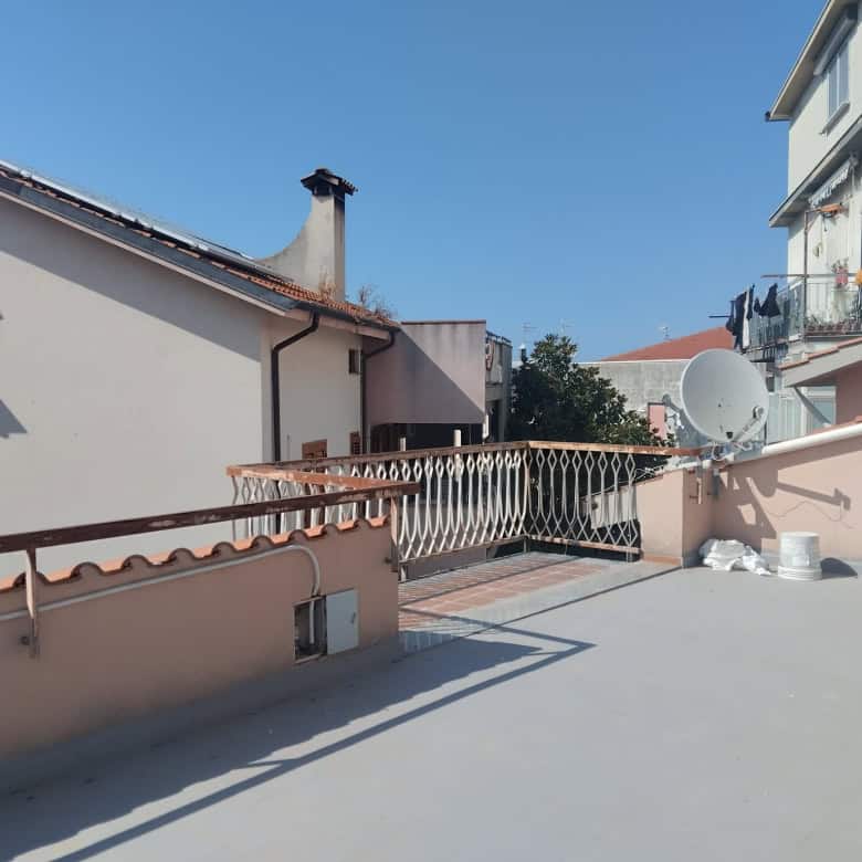 Ampio terrazzo con vista su case residenziali, parapetto in metallo e satellite, pavimentazione in cemento, ideale per relax e attività all'aperto, in zona tranquilla e ben servita.