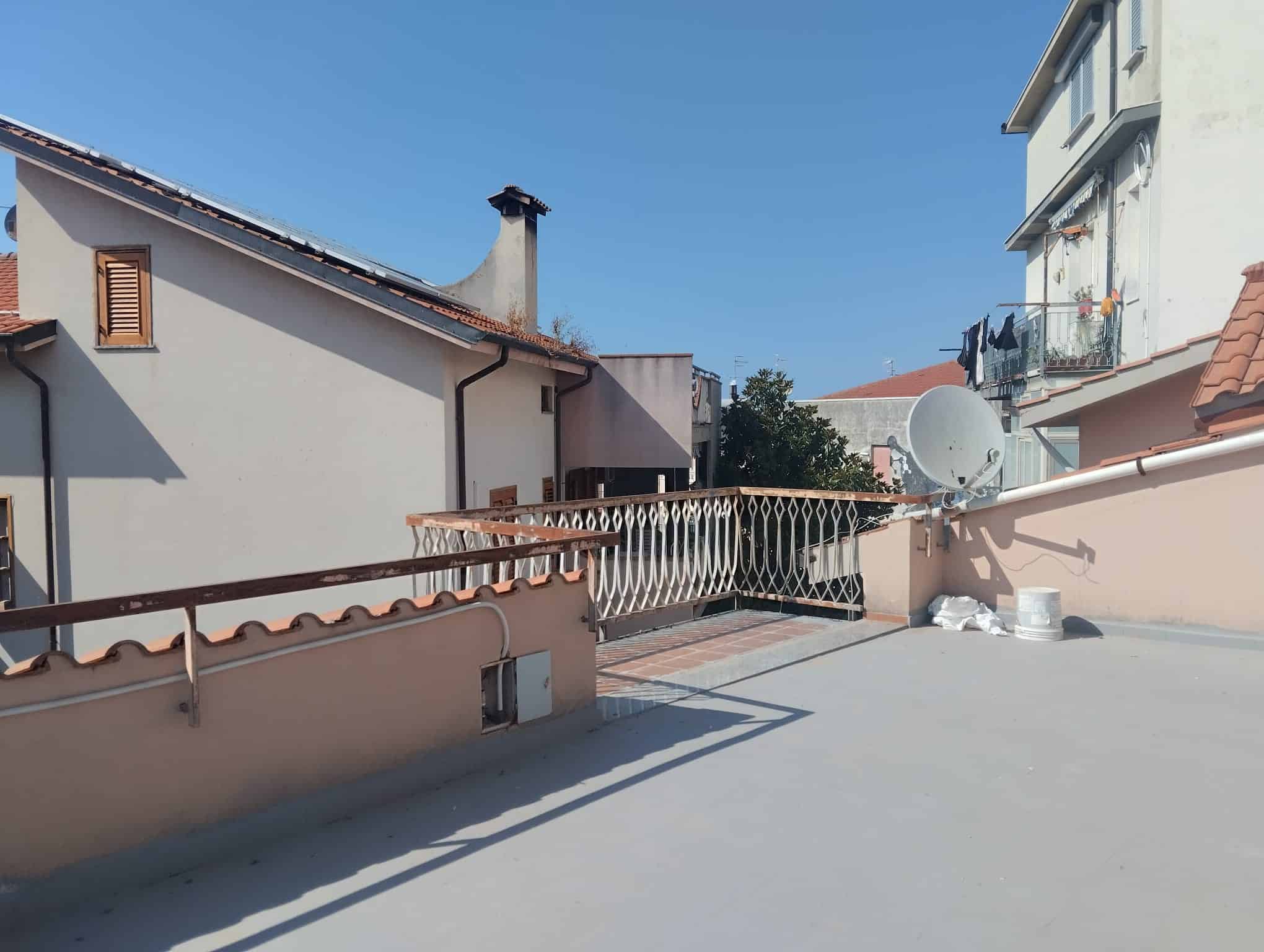 Ampio terrazzo con vista su case residenziali, parapetto in metallo e satellite, pavimentazione in cemento, ideale per relax e attività all'aperto, in zona tranquilla e ben servita.