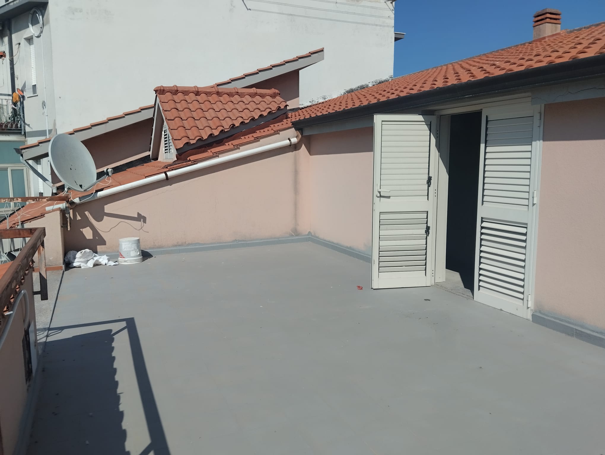 Tetto e terrazza di un appartamento con vista sul cielo, con pareti in tinta rosa e tetto in tegole rosse, spazio esterno con accesso tramite porte a persiana bianca, ideale per relax e attività all'a.