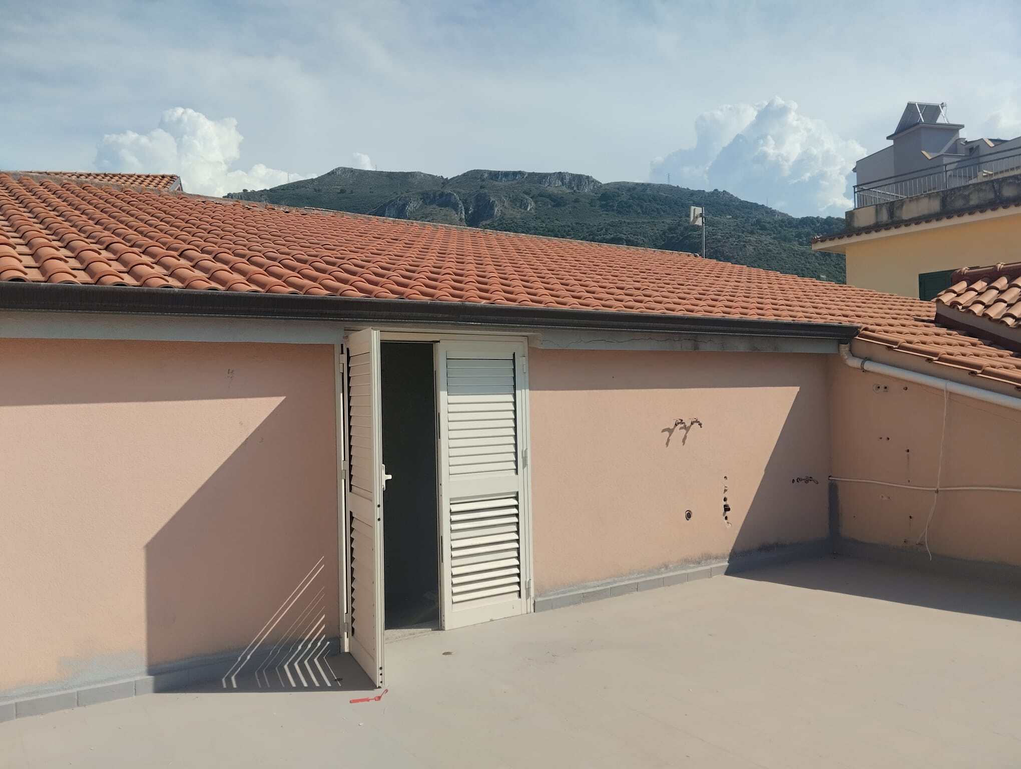 Vista panoramica di un terrazzo con porta finestra e tetto in tegole rosse, ideale per appartamenti e case in affitto o vendita in Italia.