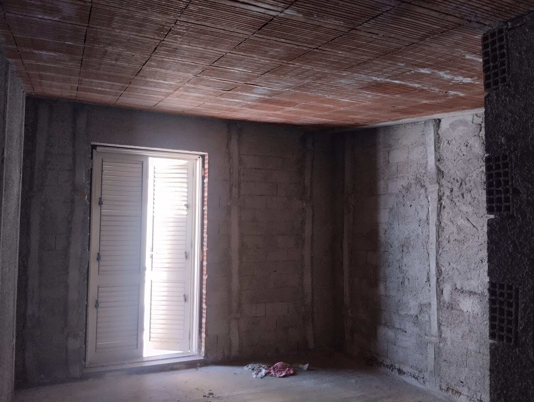 Interno di una stanza in costruzione con pareti in cemento e finestra con persiane, pronto per finiture future.