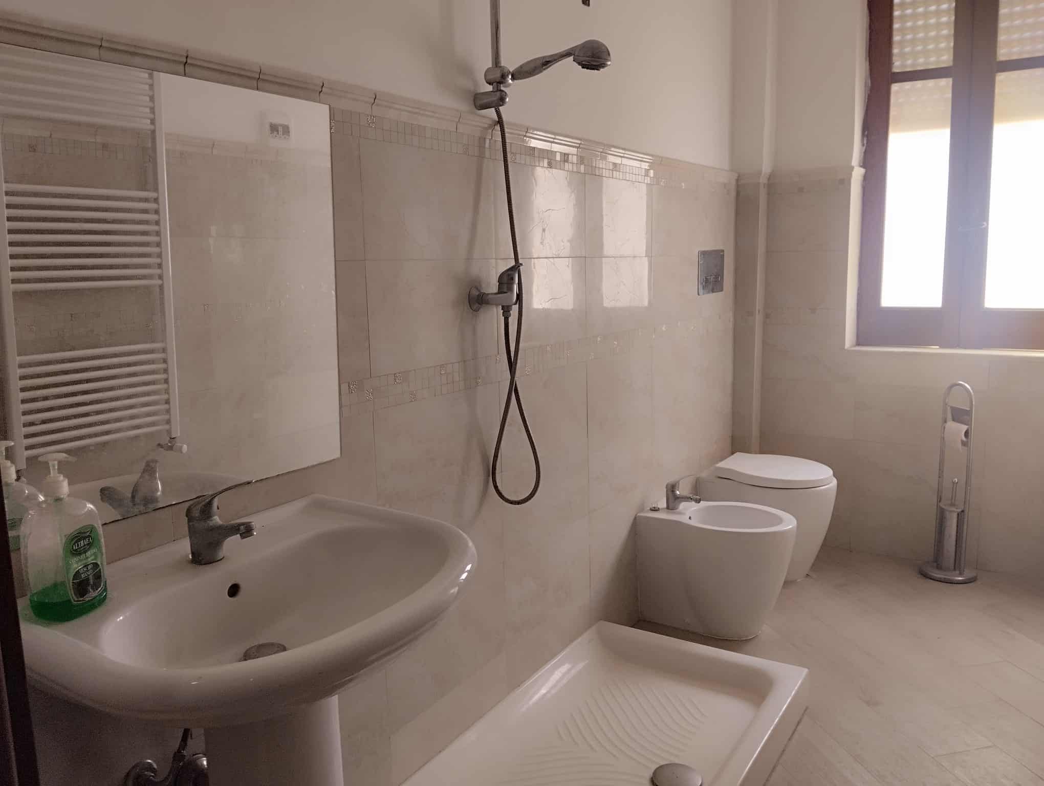 Lavabo e servizi igienici moderni in un bagno luminoso con pareti in piastrelle beige e finestra grande per illuminazione naturale.