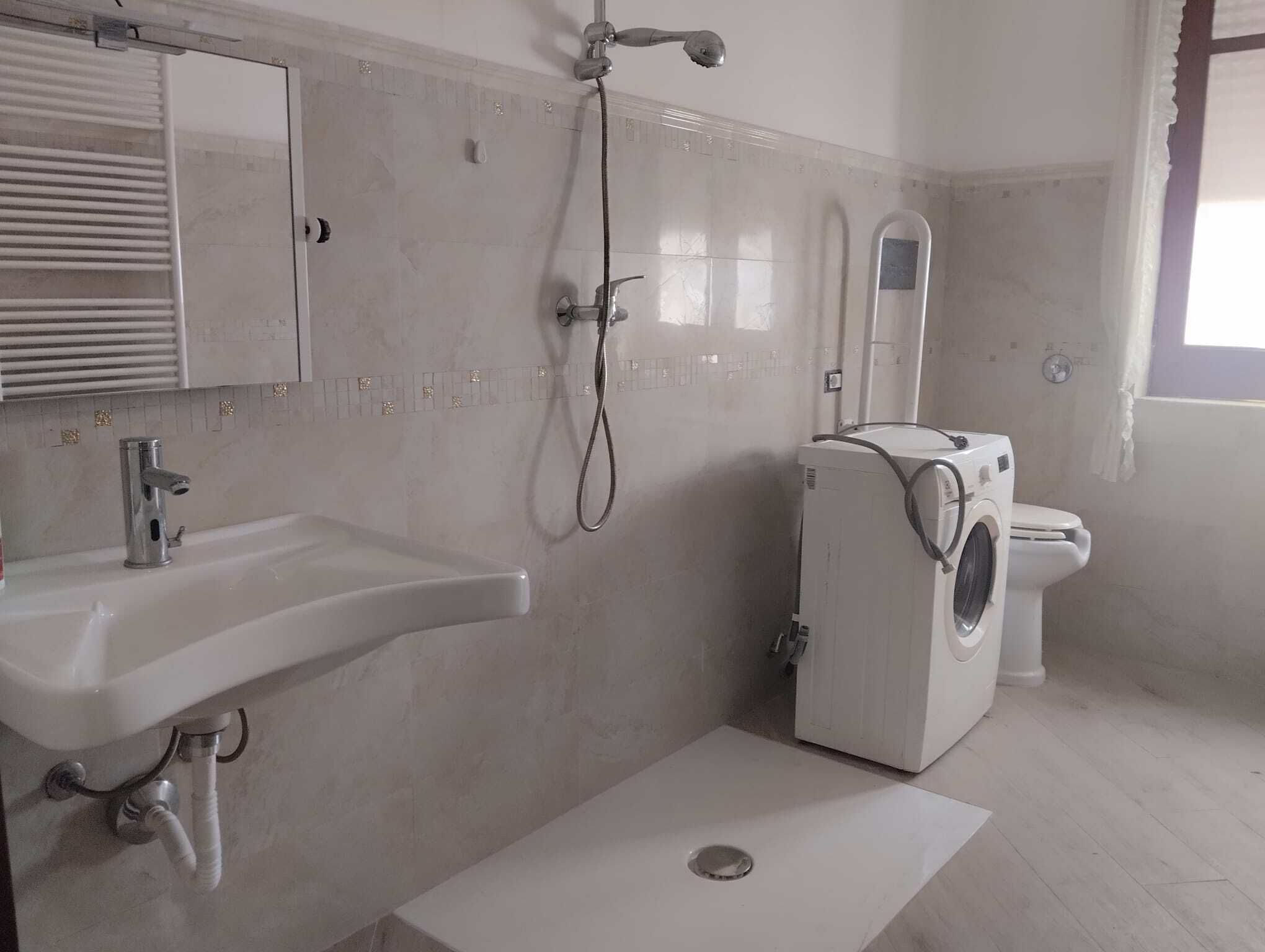 Lavatrice in bagno con doccia, lavabo e servizi igienici, ambiente luminoso e moderno, ideale per appartamenti in affitto o residenze temporanee, con spazio funzionale e arredi essenziali.