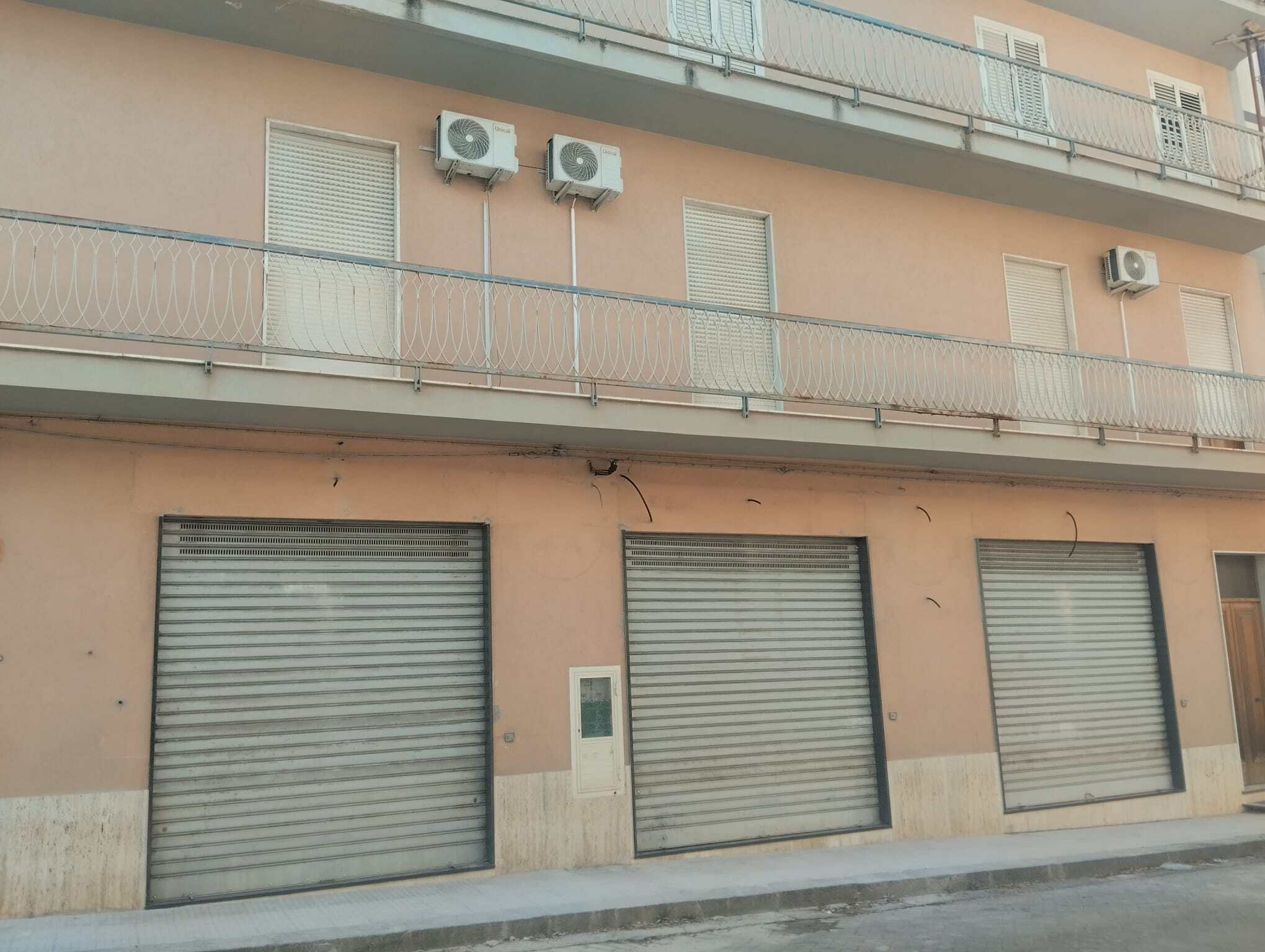 Vetrine chiuse con saracinesche in un edificio residenziale, con aria condizionata installata sulla facciata, in un contesto urbano.