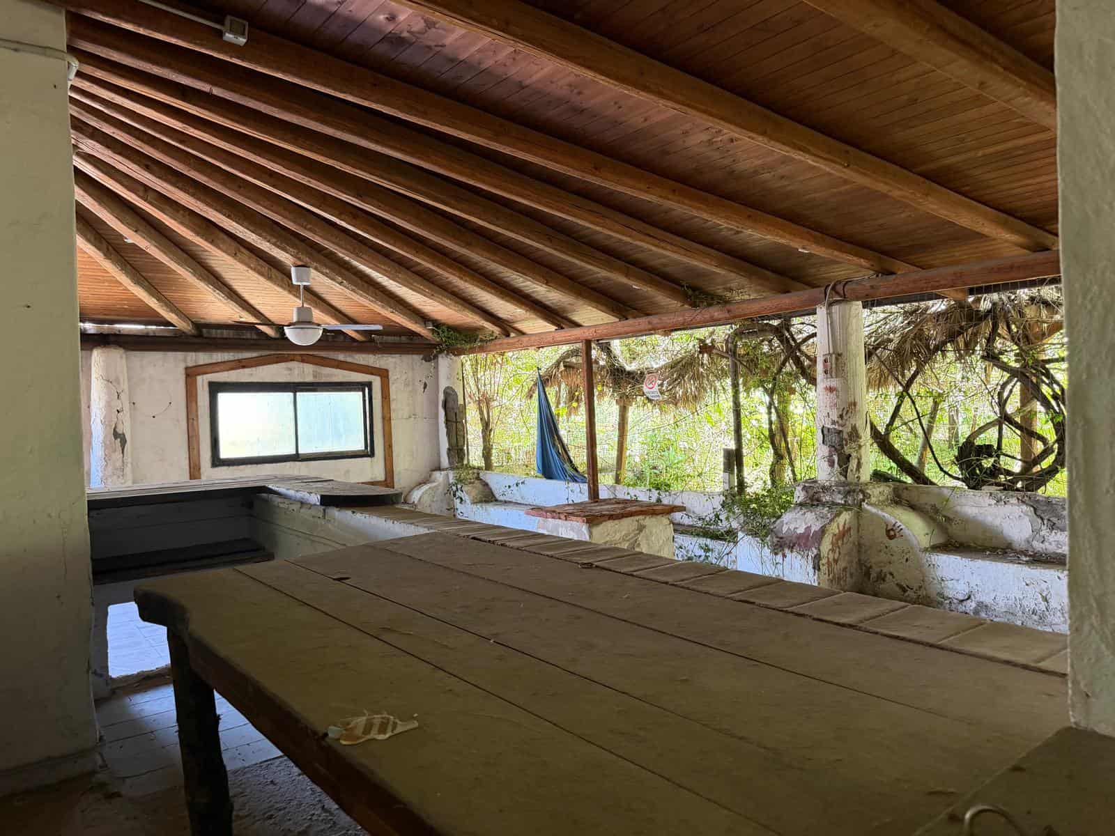 Un ambiente rustico e accogliente con soffitto in legno, spazio aperto e vista sulla natura, ideale per relax e socializzazione in una casa di campagna o rifugio immerso nel verde.