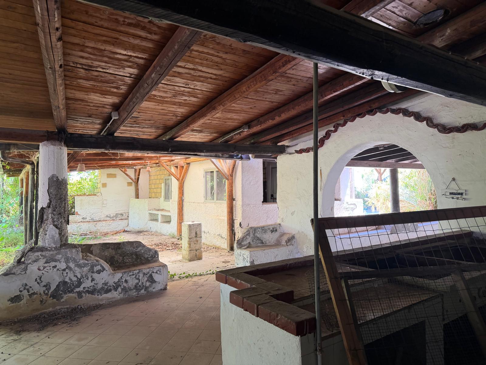 Ampia area esterna coperta con soffitto in legno, ideale per relax e socializzazione, con elementi di arredo rustici e strutture in pietra, perfetta per ambienti esterni di case o agriturismi.