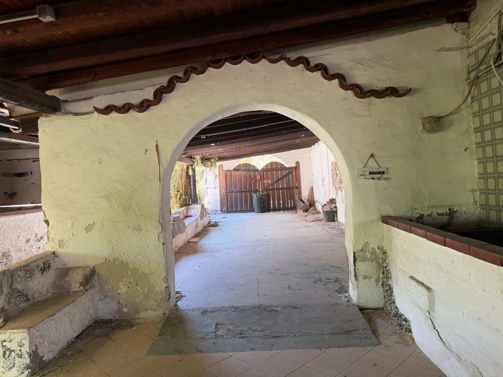 Arco in pietra con decorazioni in terracotta, ingresso di una casa rustica con pareti bianche e pavimento in piastrelle, ambiente esterno accogliente e tradizionale.