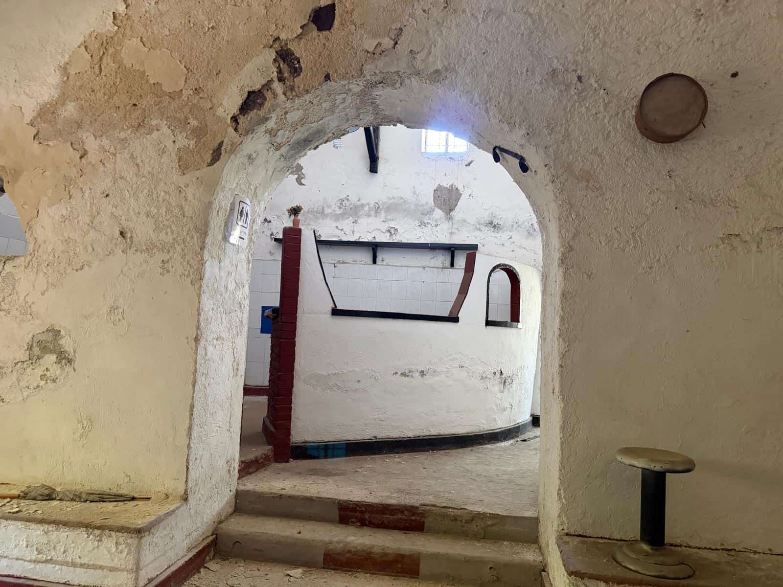 Interno di una casa rustica con pareti bianche, arco in pietra e dettagli in legno, ambiente accogliente e caratteristico.