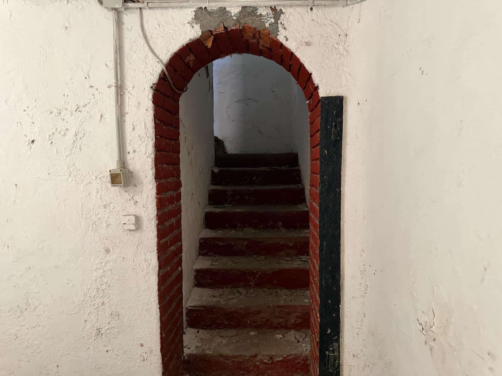 Antico ingresso con scala in pietra e arco in mattoni rossi, pareti bianche con texture rustica, ambiente interno di stile tradizionale.