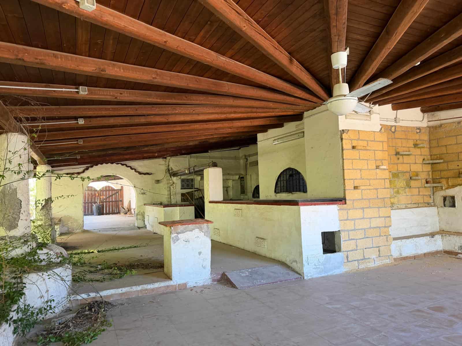 Piattaforma esterna con soffitto in legno, pareti in pietra e mattoni, ideale per relax e socializzazione all'aperto, con ventilatore a soffitto e spazio per barbecue o tavoli.