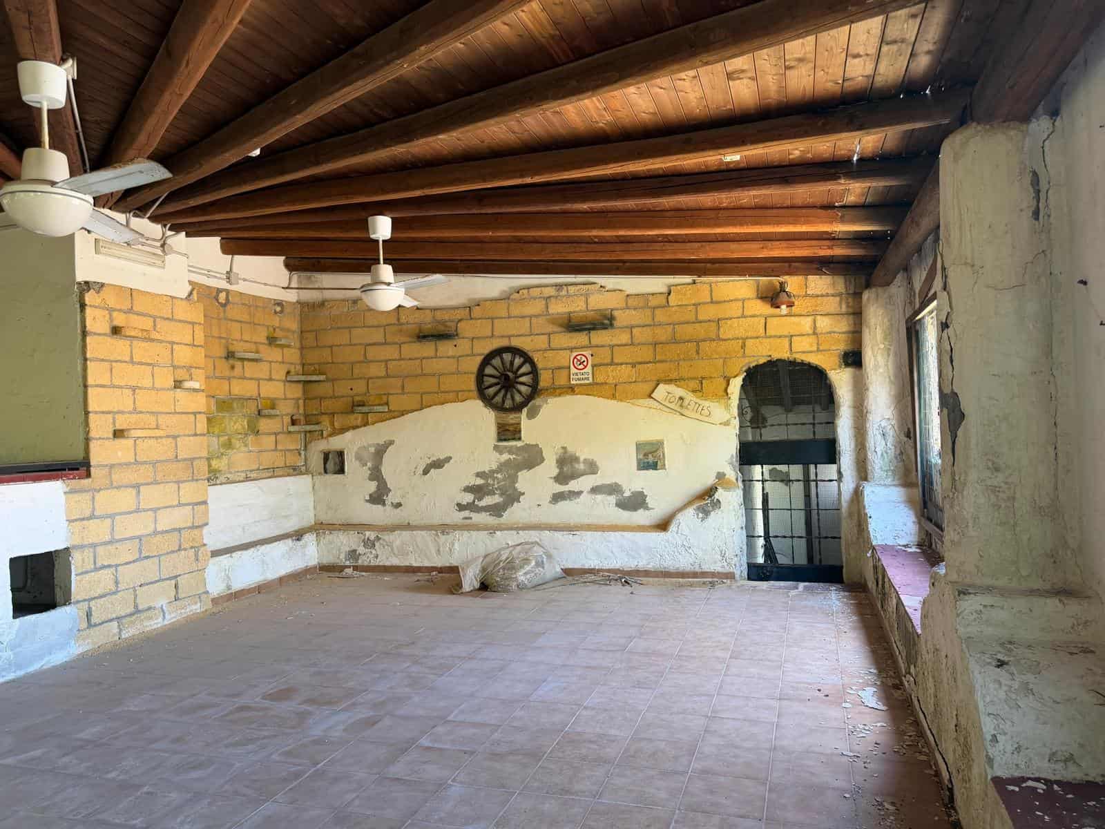 Ampio spazio interno con soffitto in legno, pareti in mattoni e grandi finestre, ideale per ristrutturazione o uso come locale commerciale o abitativo. Atmosfera rustica e autentica, perfetta per prog.