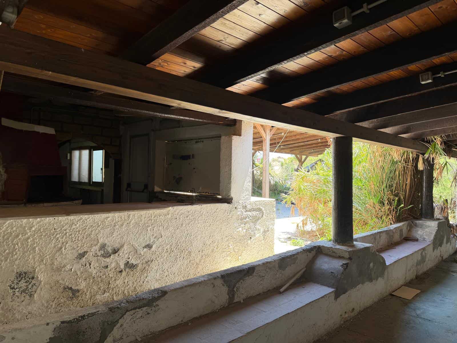 Una terrazza esterna con vista su un giardino verde, coperta da un tetto in legno, con pareti in pietra e un ambiente rustico ideale per relax e convivialità all'aperto.