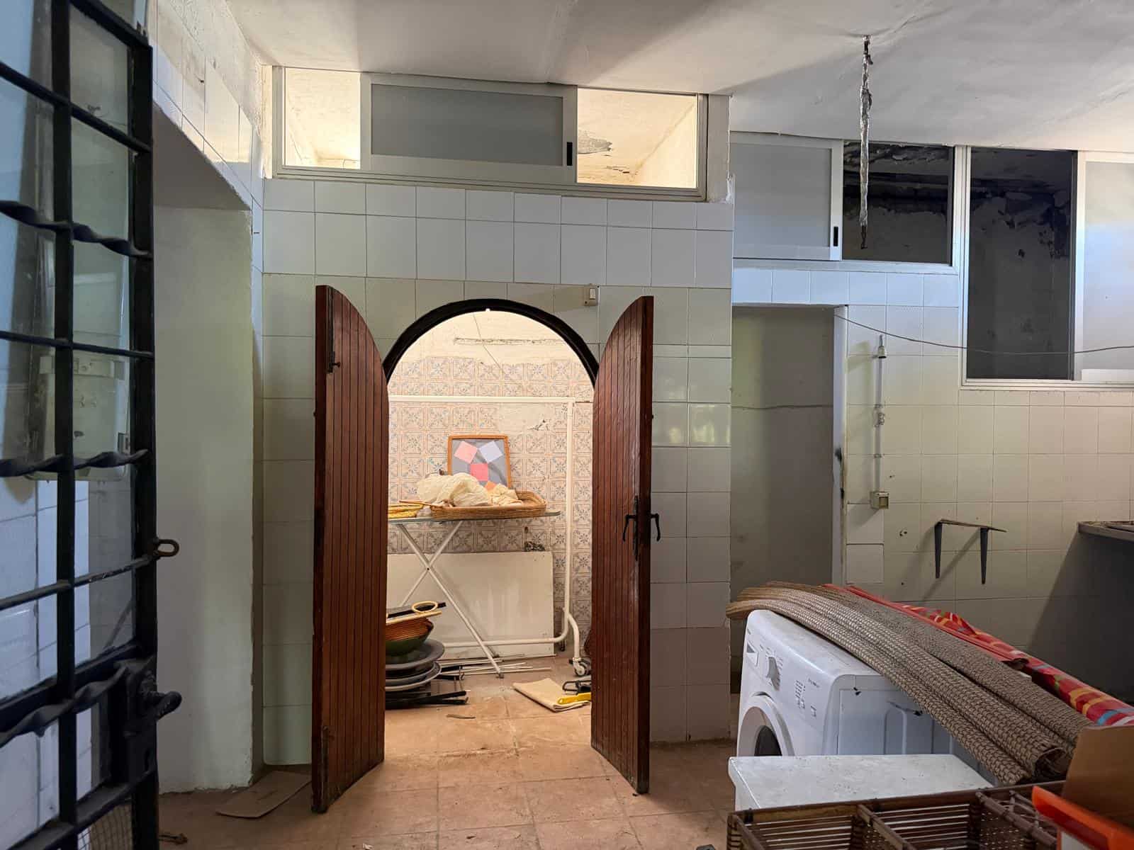 Porta in legno aperta che conduce a una stanza con pareti in mattoni e oggetti domestici, ambiente interno di una casa in fase di ristrutturazione o arredamento.