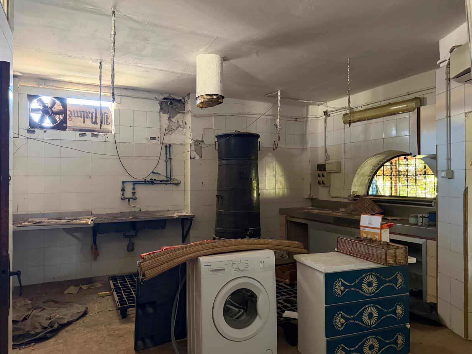 Lavanderia industriale con lavatrice, piani di lavoro in ceramica e sistema di ventilazione, ambiente funzionale e pratico per il lavaggio e la gestione dei tessuti. Spazio dedicato alle attività di p.
