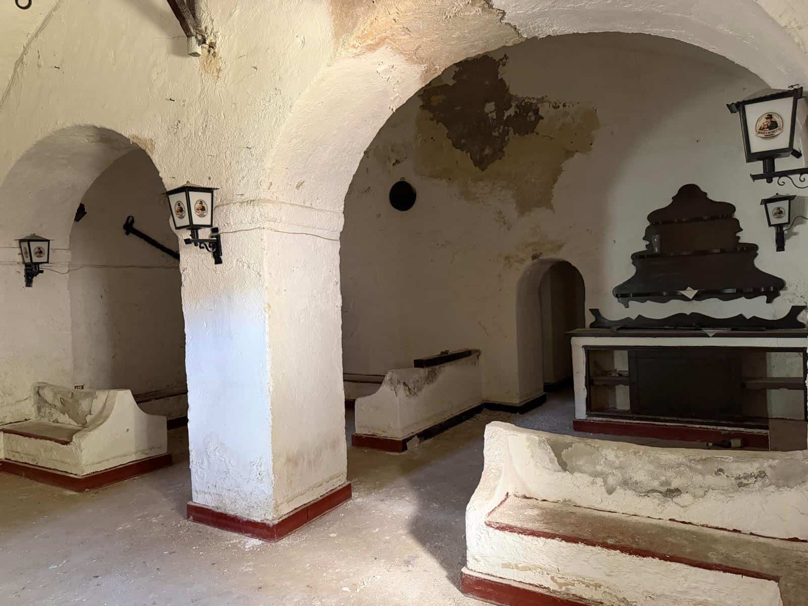 Antica cantina in pietra con archi e arredi in stile rustico, illuminata da lanterne tradizionali, perfetta per un'atmosfera autentica e accogliente.