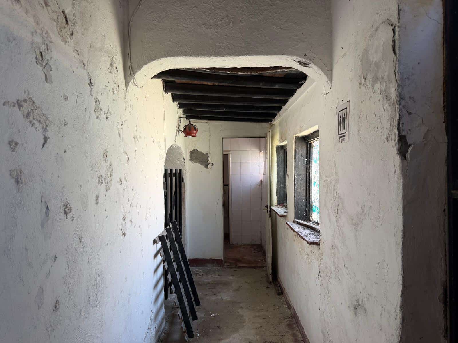 Corridoio interno di una casa in ristrutturazione con pareti bianche usurate e finestre piccole, ambiente rustico e in fase di restauro.