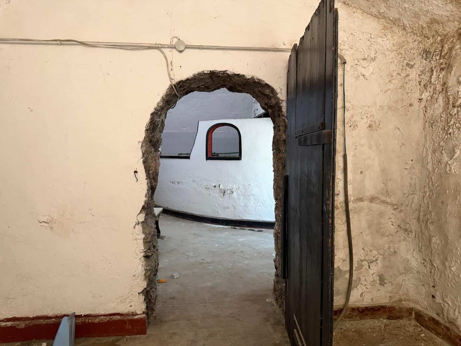 Il cancello in ferro nero aperto su un cortile interno con pareti in pietra e un arco in pietra grezza, in un ambiente rustico e storico.