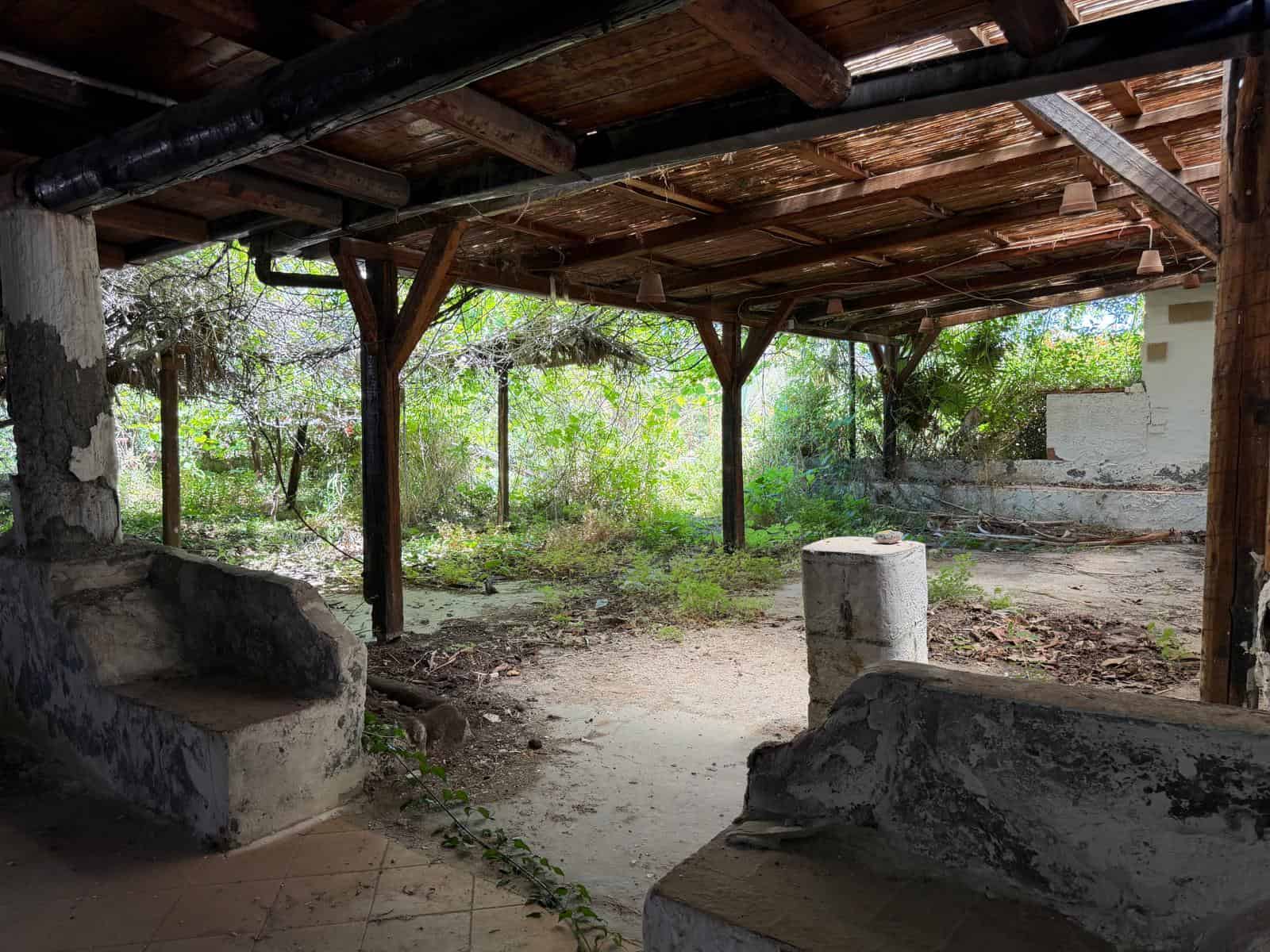 Antico spazio esterno coperto con struttura in legno e pietra, ambiente rustico e naturale ideale per relax e convivialità all'aperto.