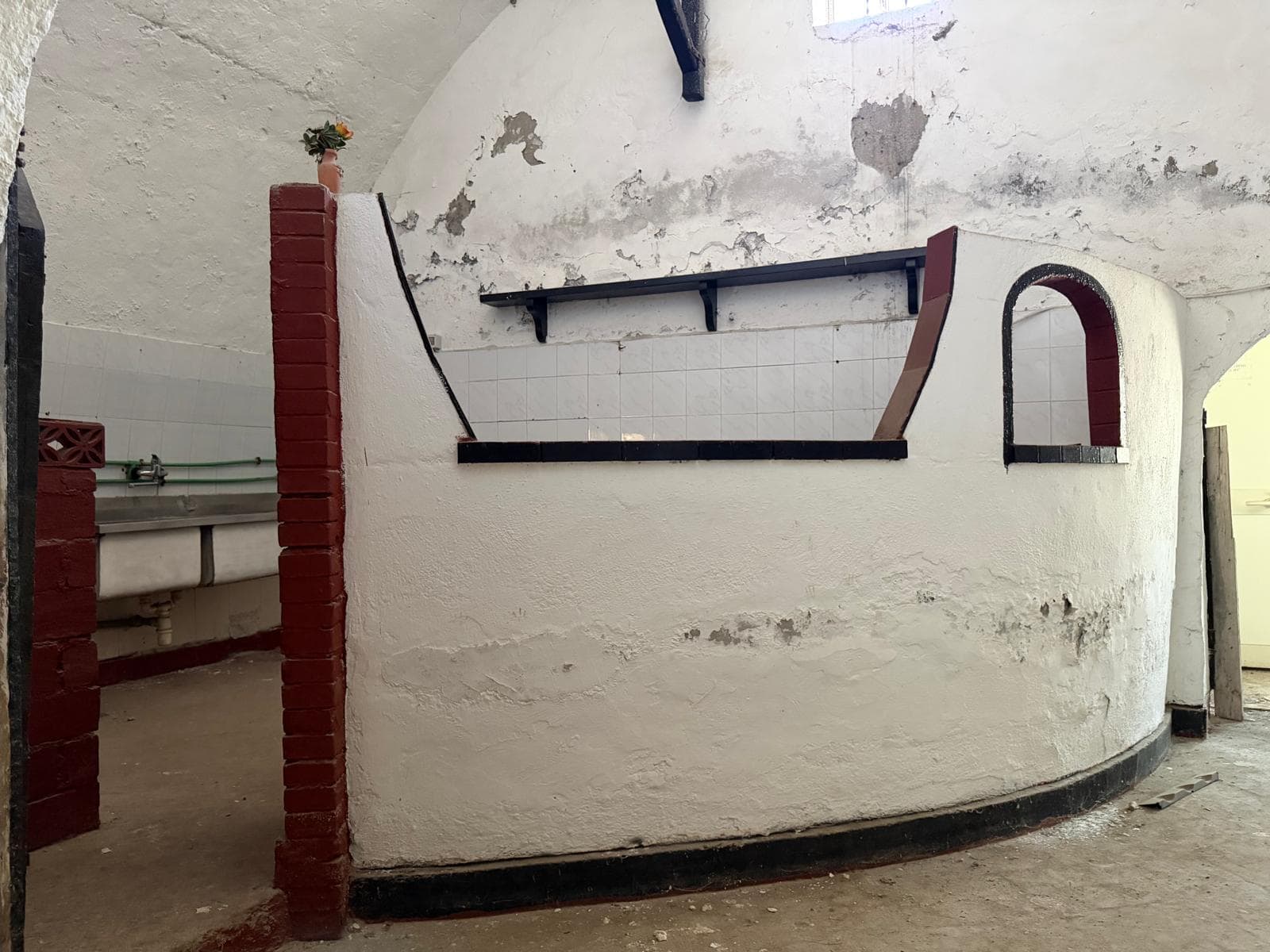 Un bancone in pietra bianca con dettagli in mattoni rossi, situato in un ambiente rustico con pareti in pietra e soffitto curvo, ideale per un bar o un'area di accoglienza.