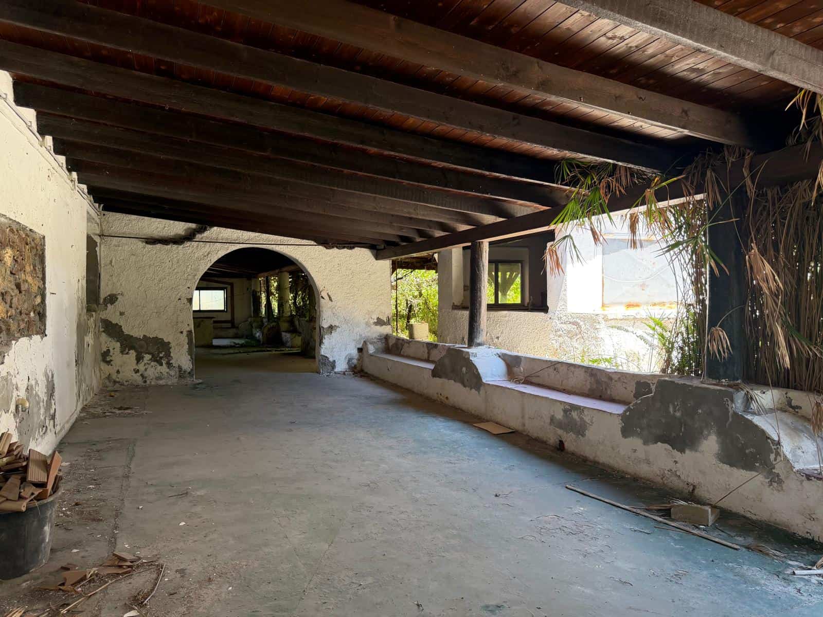 Un'immagine di un terrazzo o veranda rustica con soffitto in legno e pareti in pietra, che mostra un ambiente esterno con elementi naturali e un'atmosfera tradizionale e accogliente.