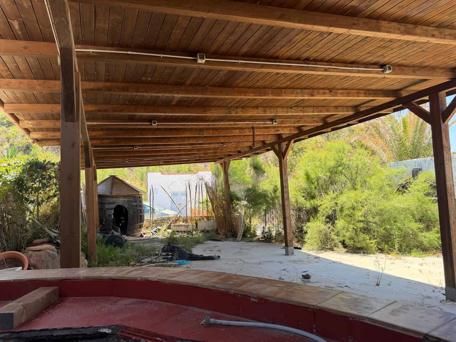 Aggiungi una copertura in legno su un'area esterna con vista su giardino e vegetazione, ideale per relax e socializzazione all'aperto. Struttura robusta e naturale, perfetta per spazi esterni di case.