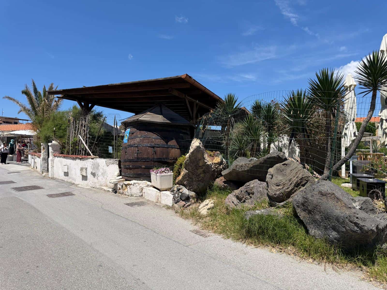 Ampia area esterna con grandi rocce e piante tropicali, struttura in legno e recinzione in metallo, ambiente naturale e accogliente, ideale per relax e socializzazione all'aperto.