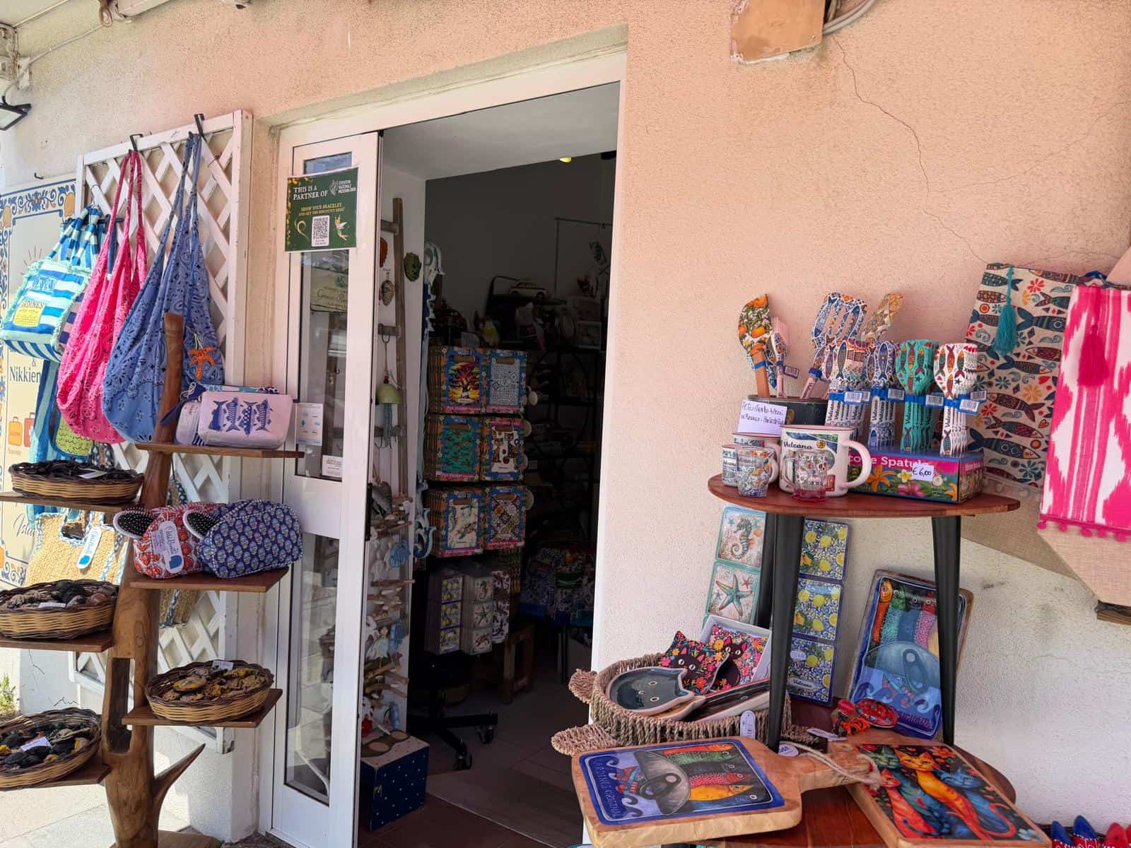 Tende e accessori per la casa esposti all'esterno di un negozio NextCasa, con prodotti colorati e decorativi, tra cui borse, tessuti e oggetti artigianali, in un ambiente accogliente e vivace.
