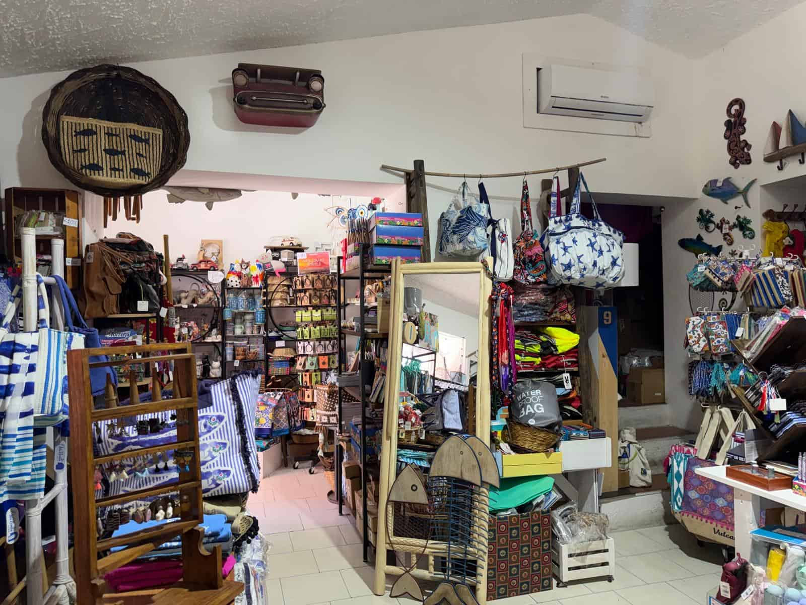 Borsa di paglia e accessori colorati in un negozio di souvenir e articoli da regalo, con espositori pieni di prodotti vari e decorazioni vivaci.